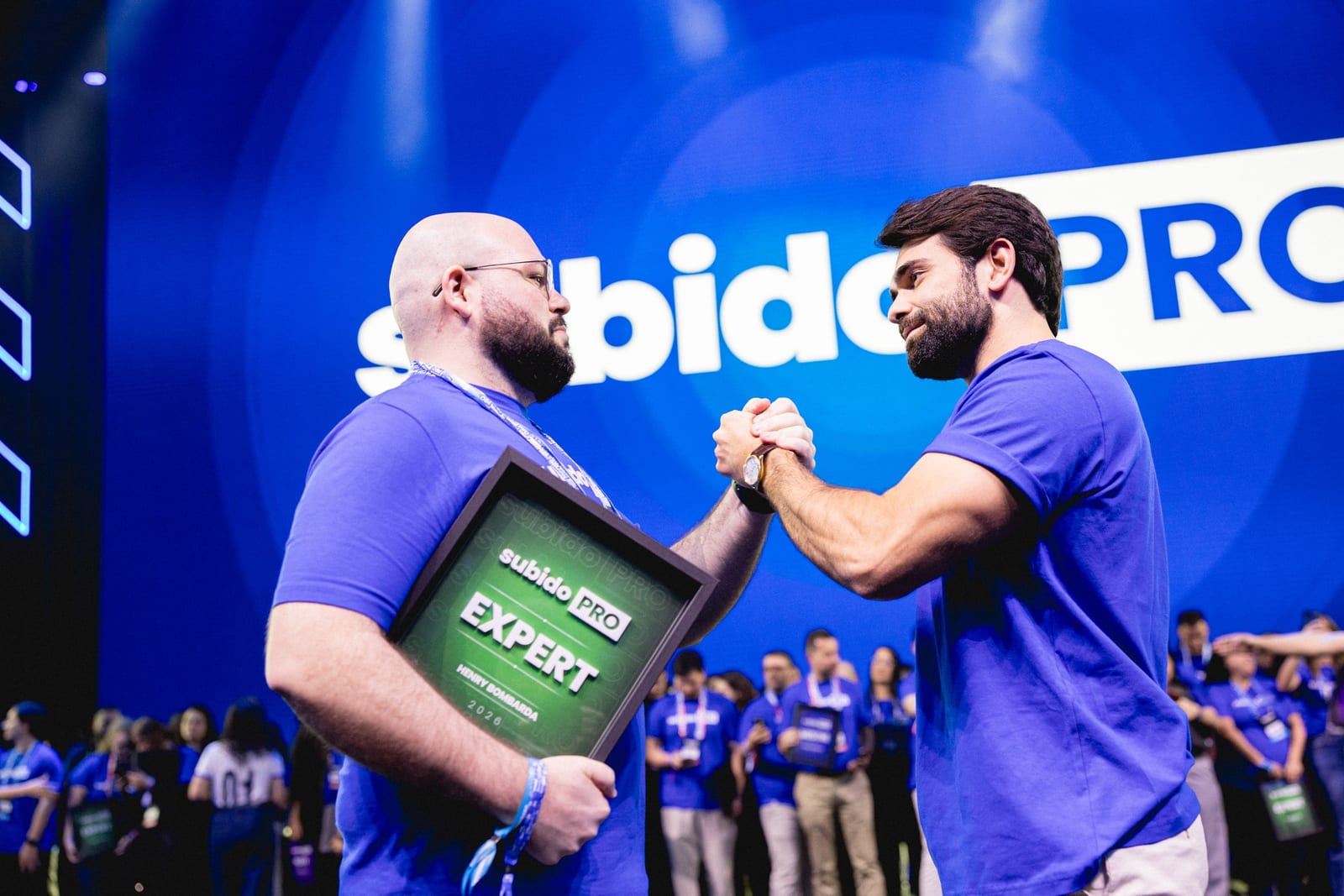 Henry Bombarda segurando o certificado Expert do SubidoPRO e apertando a mão de Pedro Sobral no palco do evento